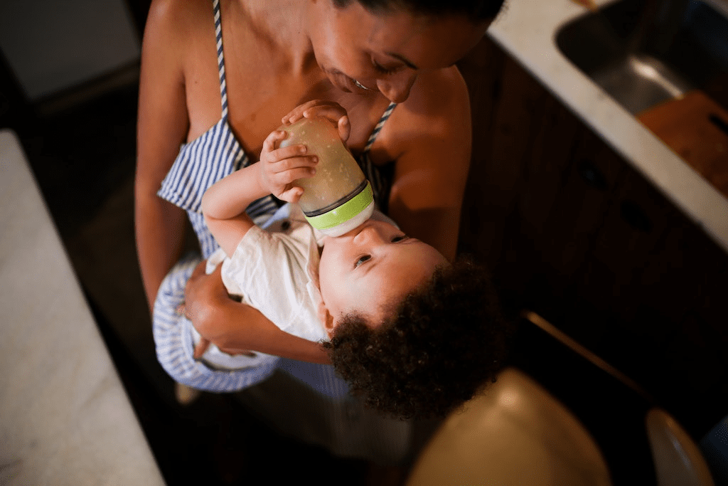 Uma mãe alimentando o bebê com mamadeira enquanto o carrega.