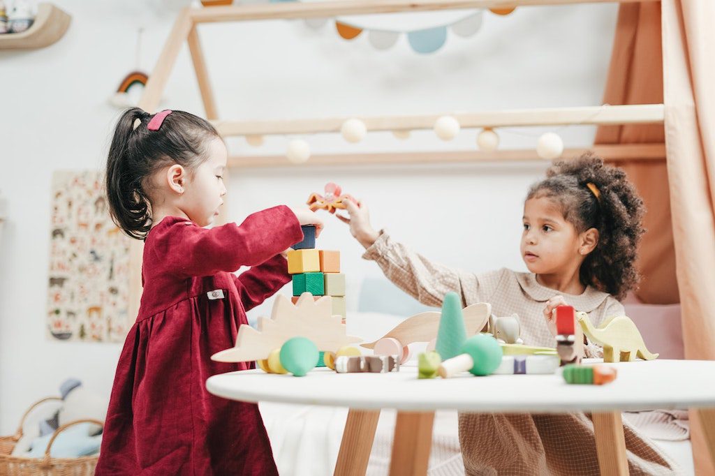Crianças de até 2 anos brincando com brinquedos educativos em uma mesa branca.