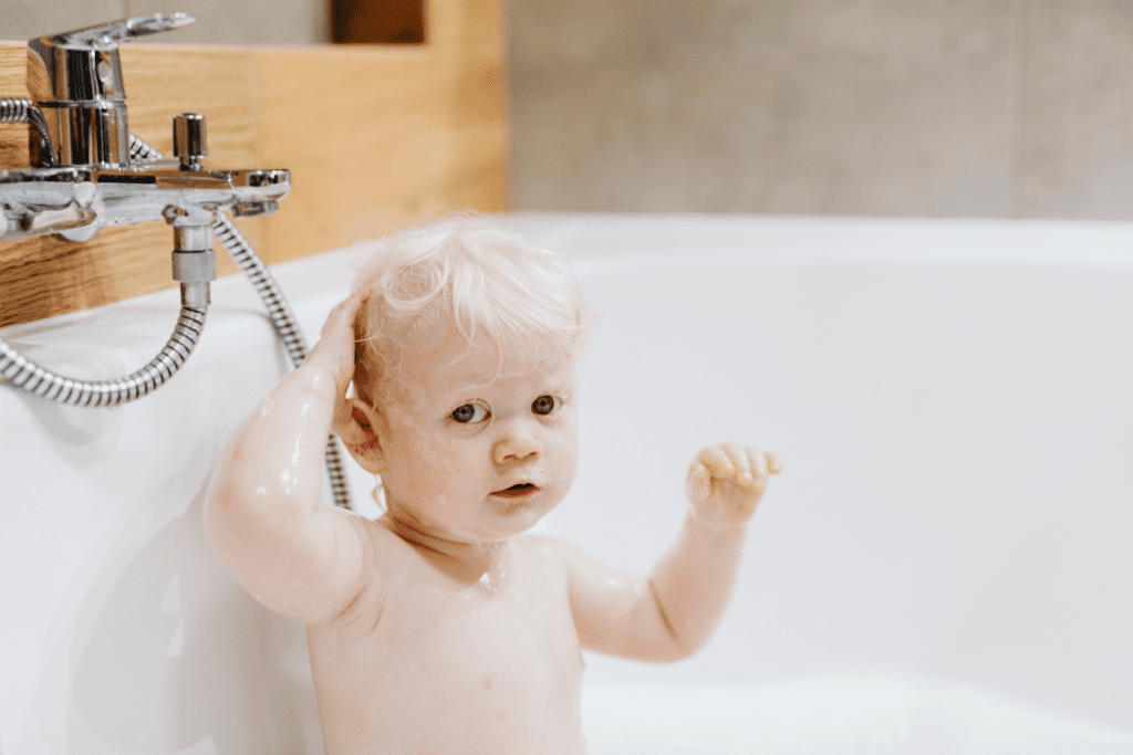 Uma criança lavando cabelo com shampoo infantil em uma banheira.