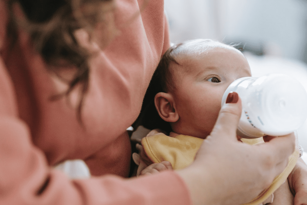 Mãe alimentando bebê com leite de uma mamadeira.