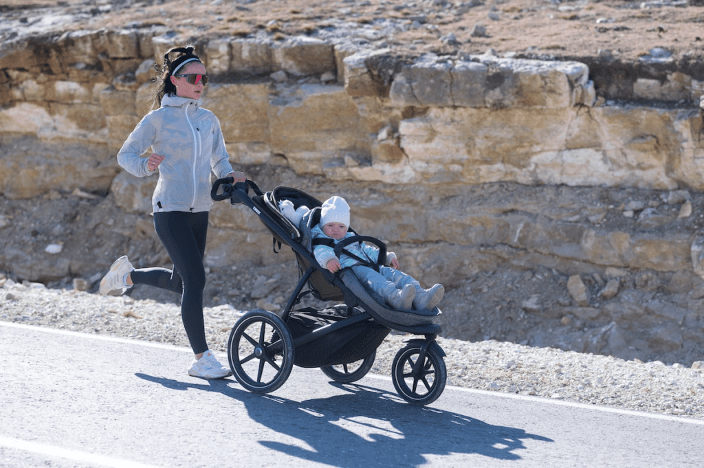 Mulher no sportswear correndo com carrinho de bebê 3 rodas.