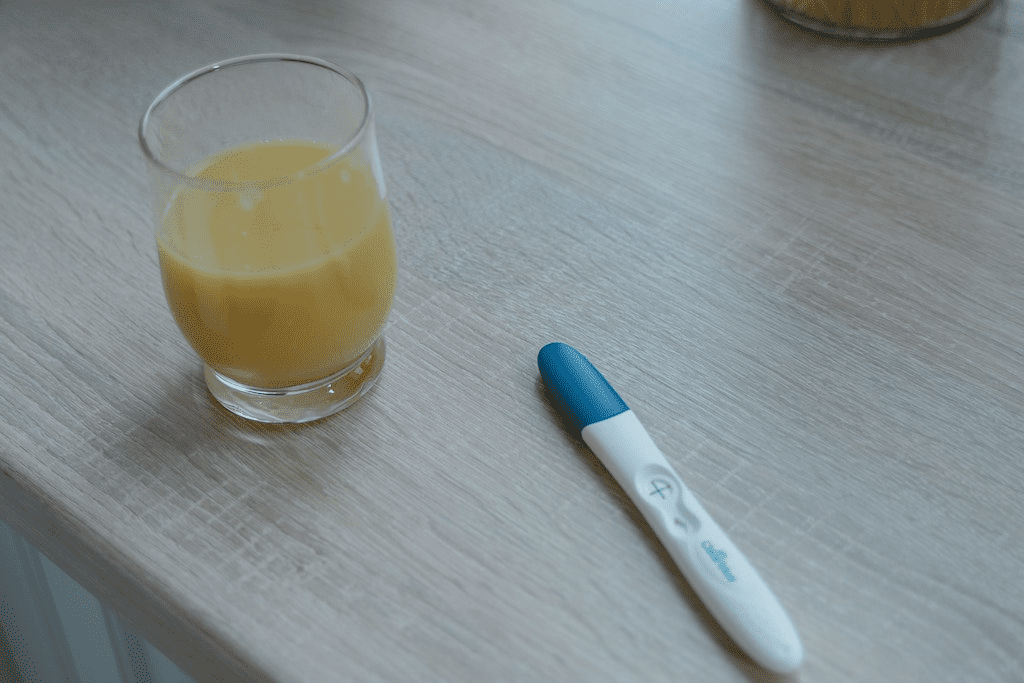 Um copo transparente perto do teste de gravidez em uma mesa de madeira.