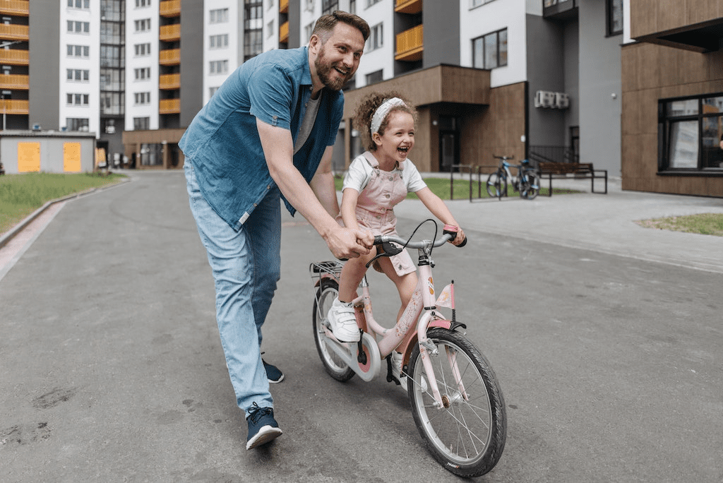 Pai guiando sua filha enquanto ela aprende a andar de bicicleta.