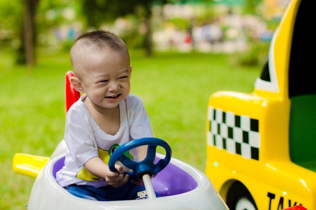 Menino sorrindo sentado em um pequeno quadriciclo infantil.