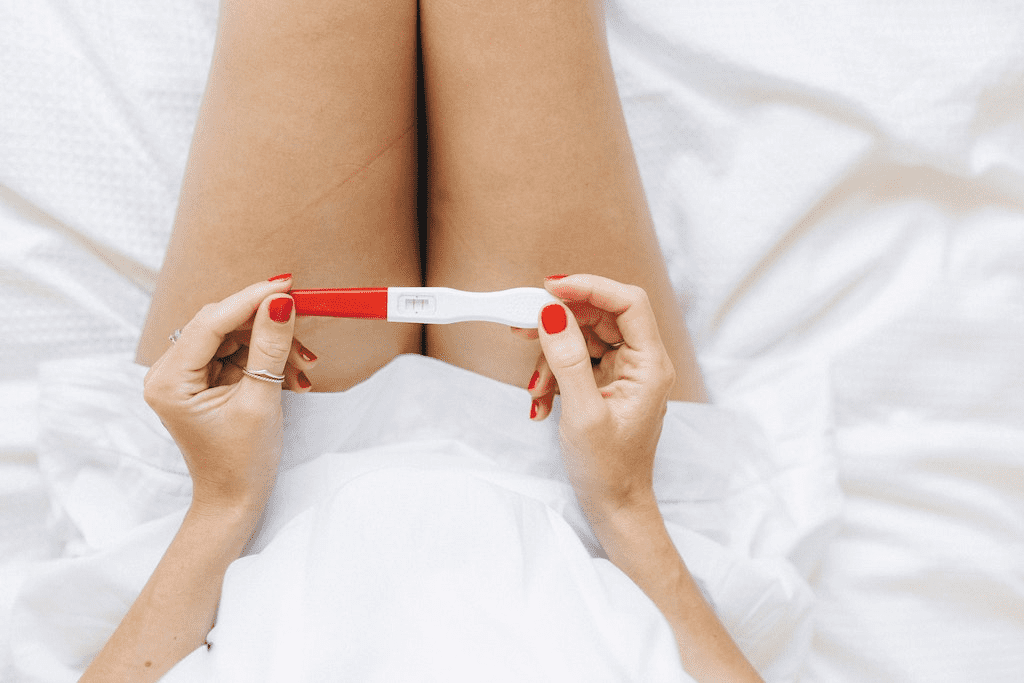 Mulher com unhas feitas de vermelho segurando um teste de gravidez.