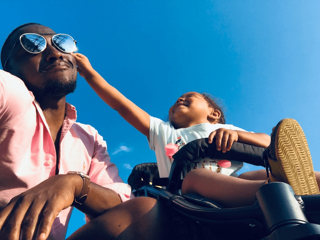 Uma criança tocando o rosto do pai enquanto está em um carrinho de bebê com 3 rodas.