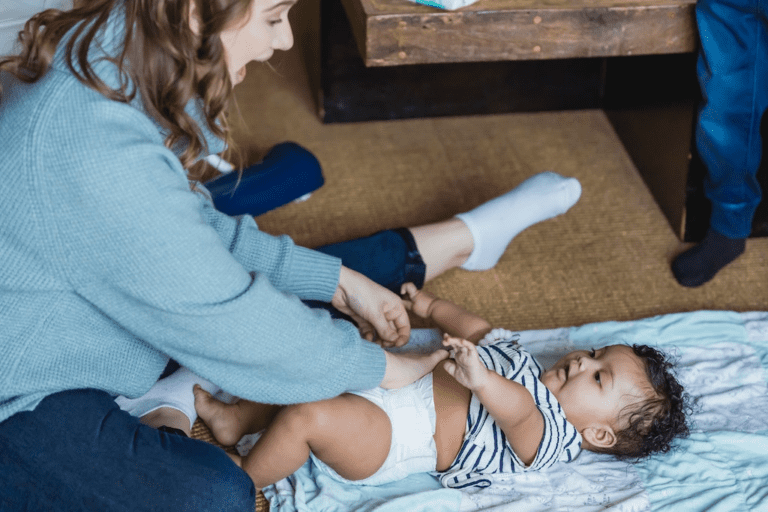 Mãe alegre brincando com seu bebê fofo enquanto troca a fralda descartavel.